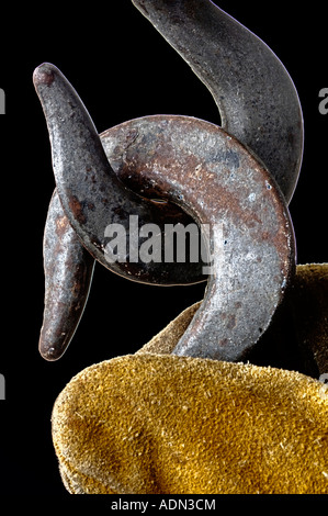 gloved hand of worker holding heavy duty steel hooks hanging from construction crane Stock Photo