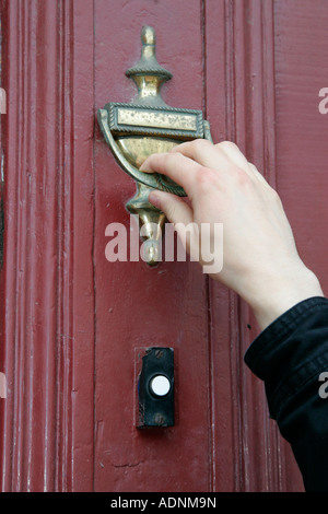 mans hand using door knocker on wooden door instead of bell cold calling household Stock Photo