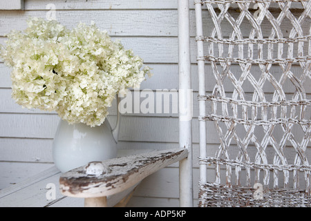 White hydrangeas in pitcher on front porch with rocking chair Stock Photo