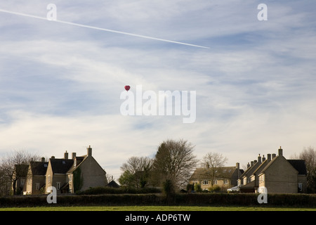 Hot air balloon flies over village of Little Rissington Gloucestershire United Kingdom Stock Photo