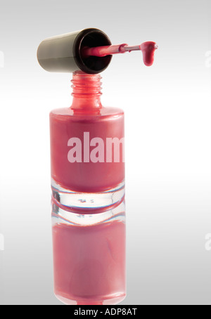 Nail Polish dripping from a nail varnish brush balanced on a nail varnish bottle Pink colour against white with a reflection Stock Photo