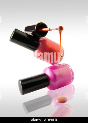 2 Nail Polish bottles balanced on each other in a fun way with a nail varnish brush balanced ontop dripping nail varnish Stock Photo