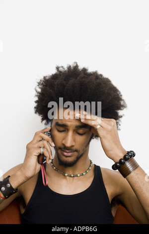 Man with afro and bracelets talking on cell phone with hand on head Stock Photo