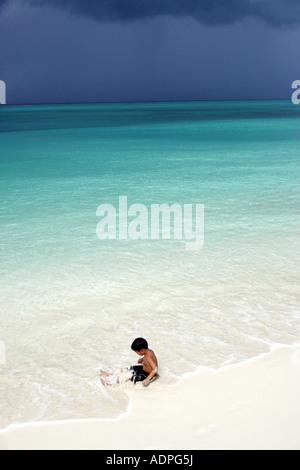 Boy sitting in the surf Turk and Caicos Islands Caribbean with dark clouds gathering Stock Photo
