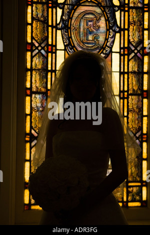 Traditionally dressed bride holding floral bouquet in front of stainglass window inside church Stock Photo