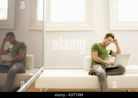 Pensive man using laptop on modern sofa in modern apartment Stock Photo