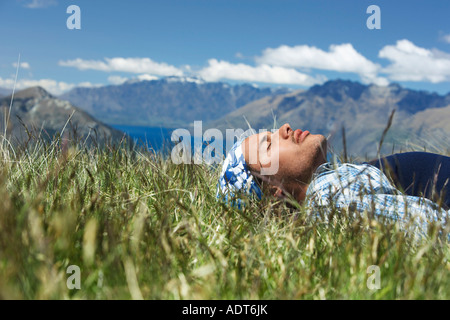 Man lying in field by lake and hills Stock Photo