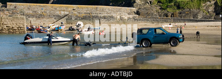 Gorran Haven beach & harbour wall men with 4x4 car & trailer hooking winch for loading speed boat at waters edge on firm sand Cornwall England UK Stock Photo