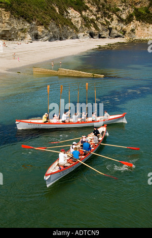 Winners hold oars aloft two mixed teams of long pilot gig row boats return to Charlestown shoreline after race out to sea & back Cornwall England UK Stock Photo