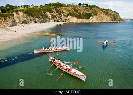 Winners hold oars aloft three mixed teams of long pilot gig row boats return to Charlestown shoreline after race out to sea & back Cornwall England UK Stock Photo