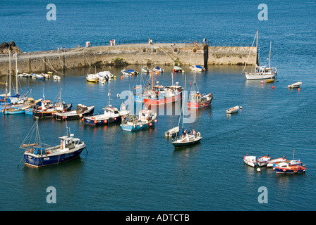 Mevagissey fishing village looking down on part of harbour and wall as sailing yacht enters port under motor power Cornwall England UK Stock Photo