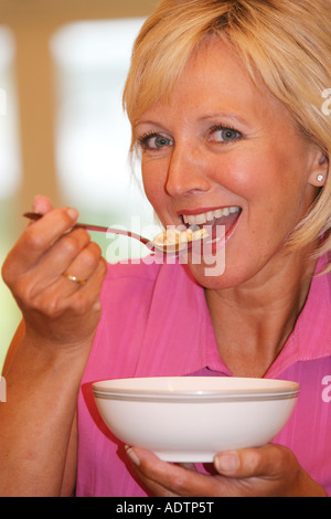 Mature Middle Aged Woman Sitting Alone Eating And Enjoying A Bowl Of Healthy Breakfast Cereals In A Home Environment Wearing A Pink Top Stock Photo