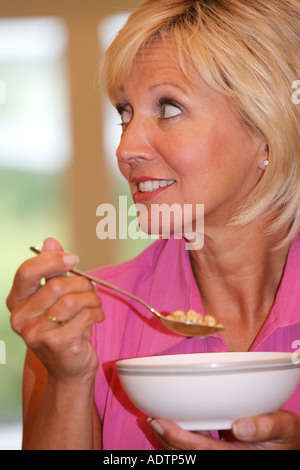 Mature Middle Aged Woman Sitting Alone Eating And Enjoying A Bowl Of Healthy Breakfast Cereals In A Home Environment Wearing A Pink Top Stock Photo