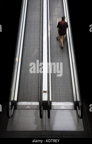 man pushing trolley on an escalator Stock Photo