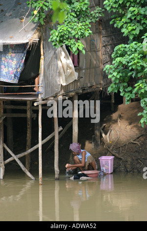 A Cambodian woman washes clothes in the dirty muddy polluted river of Siem Reap Cambodia in front of her wooden family hut home Stock Photo