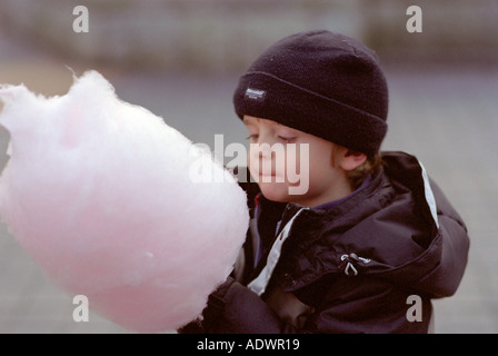 small boy in coat eating candy floss in winter at the park Stock Photo
