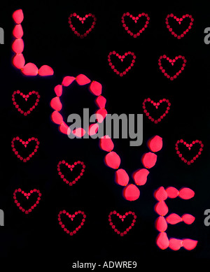 The word LOVE written in red rose petals with small hearts on black background Stock Photo