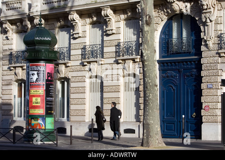 Couple walk past obelisk advertising theatre productions in Parisian street Boulevard St Germain Latin Quarter France Stock Photo