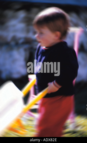 Children kid little 5 10 boy pushing toy wheelbarrow handcart handbarrow barrow cart playground people person child Stock Photo