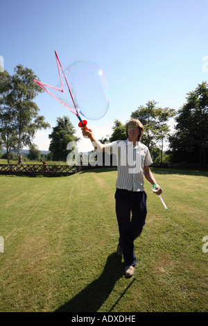 Man in mid twenty's blowing large bubbles outside using a bubble wand. Stock Photo