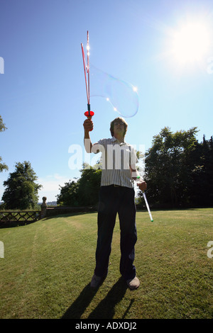 Man in mid twenty's blowing large bubbles outside using a bubble wand. Stock Photo