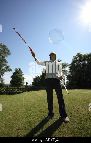 Man in mid twenty's blowing large bubbles outside using a bubble wand. Stock Photo