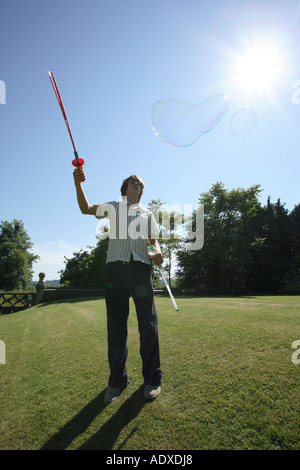 Man in mid twenty's blowing large bubbles outside using a bubble wand. Stock Photo