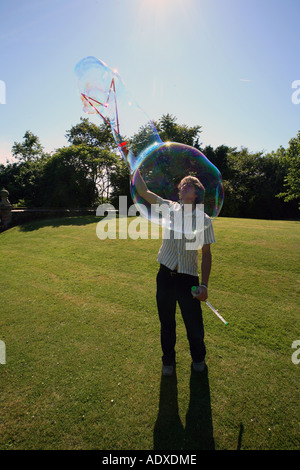 Man in mid twenty's blowing large bubbles outside using a bubble wand. Stock Photo