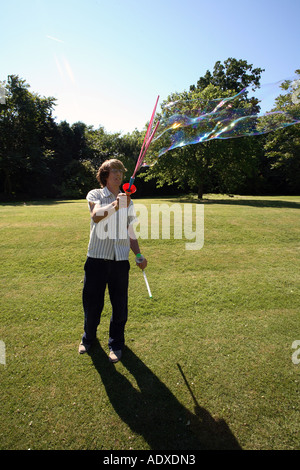Man in mid twenty's blowing large bubbles outside using a bubble wand. Stock Photo