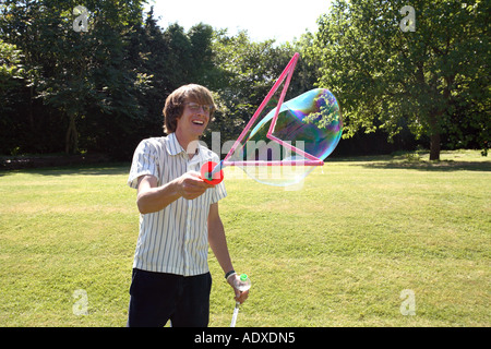 Man in mid twenty's blowing large bubbles outside using a bubble wand. Stock Photo