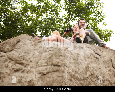 Couple sitting on rock, woman holding binoculars. low angle view Stock Photo