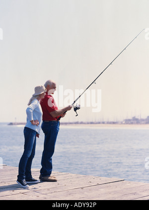 Fisherman in action. He stands in water and holds fly rod in one hand and  spoon in the other one. Also adult has a fishing net on the back. Green  Stock Photo - Alamy