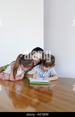 Mother assisting son (7-9) and daughter (5-6) doing homework Stock Photo