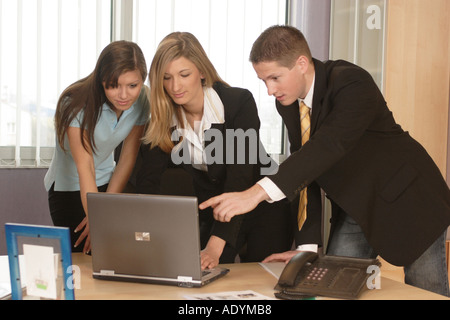 two women and man with laptop, standing behind desk . Stock Photo