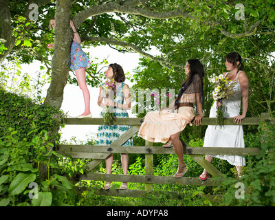 Four girls climbing over country gate in summer clothes Stock Photo