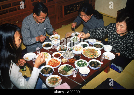 Family sitting at dinner table eating variety of home made Korean foods in South Korea