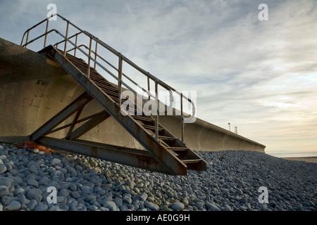 Concrete sea defence wall with iron stairway no longer reaching the ground on the south Wales coast Stock Photo