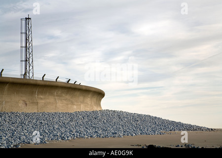 Concrete sea wall with pebbles piled up against it on a sandy beach on the south Wales coast Stock Photo