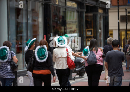 hen party of english women wearing green and white cowboy hats walks through shopping area of dublin past louis vuitton shop Stock Photo