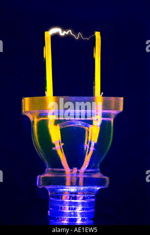 Clear blue pink and yellow electric plug against a dark blue background with sparks between the plugs Stock Photo