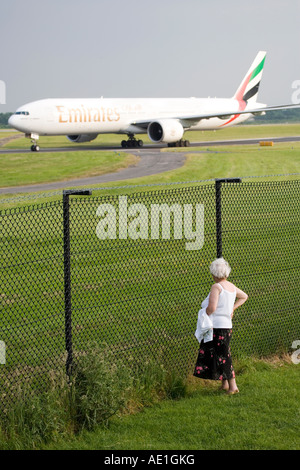 Commercial civil aviation Emirates Boeing 777 with old lady OAP looking on through fence Stock Photo