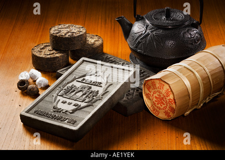 A tea kettle, tea bricks and tea rolls wrapped in fancy packaging placed on a table top. Stock Photo