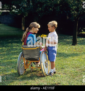 Little boy giving flowers to disabled woman in wheelchair in garden Stock Photo