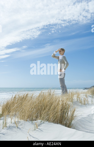 Woman standing on dune, shading eyes, smiling Stock Photo