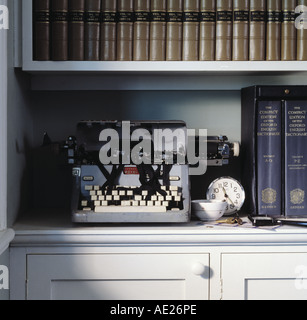 Close-up of a vintage typewriter on bookcase with leather-bound books and small clock Stock Photo