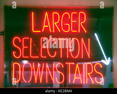 Arrow pointer and large red neon sign saying Larger Selection Downstairs Stock Photo