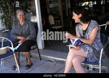 Tourist Visitor to Crete practices her Greek language with a local who is lace making in a Cafe Southern Crete Greece Stock Photo