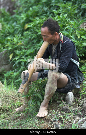 Mud splattered farmer takes break from ploughing rice terraces to smoke traditional pipe near Sapa Vietnam Stock Photo