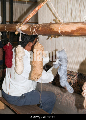 Demonstration of woollen carpet manufacture with Asian man hand knotting wool to make patterned carpet on a loom Stock Photo