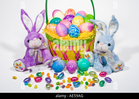 Straw Easter basket filled with colored eggs with stuffed easter bunnies and colorful candies Stock Photo